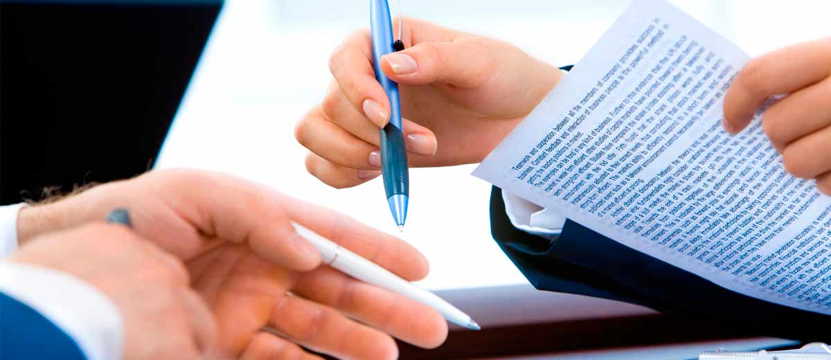 Descripción imagen: Manos de mujer y hombre sosteniendo documentos y bolígrafos.