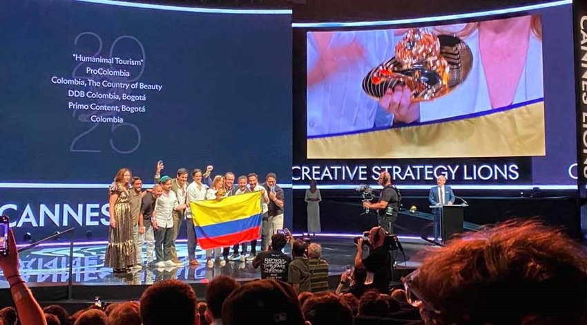 Hombres y mujeres en un escenario recibiendo un premio y sosteniendo la bandera de Colombia.