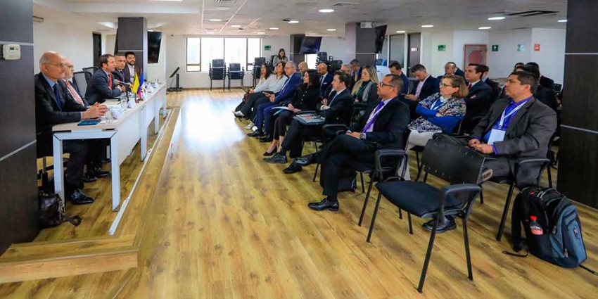 Hombres y mujeres sentados en sillas, prestando atención a los expositores al frente.