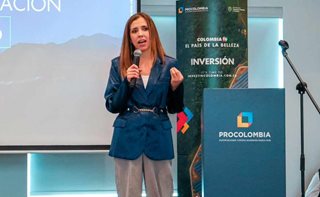 Mujer, de pie, hablando por micrófono al público desde el escenario.