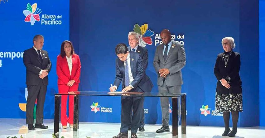 Ministro Reyes firmando documento sobre una mesa, junto con tres hombres y dos mujeres que están detrás de él.