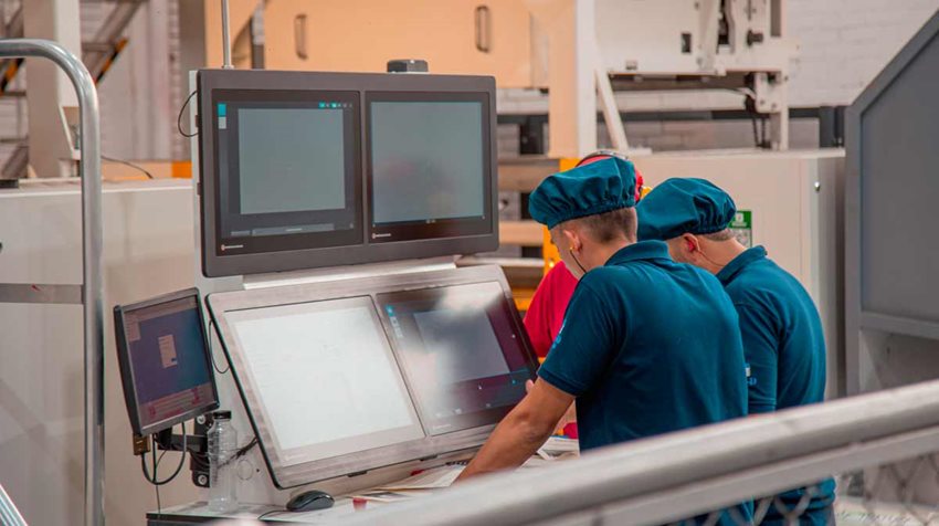 Dos hombres, con ropa y elementos de seguridad, trabajando en máquina de planta.