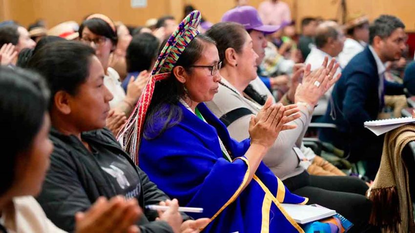Hombres y mujeres, entre ellos indígenas, aplaudiendo como público asistente.