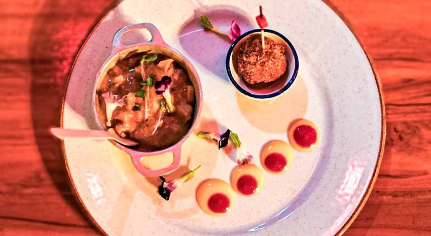 Sobre una mesa de madera, plato blanco con comida dentro de dos recipientes.