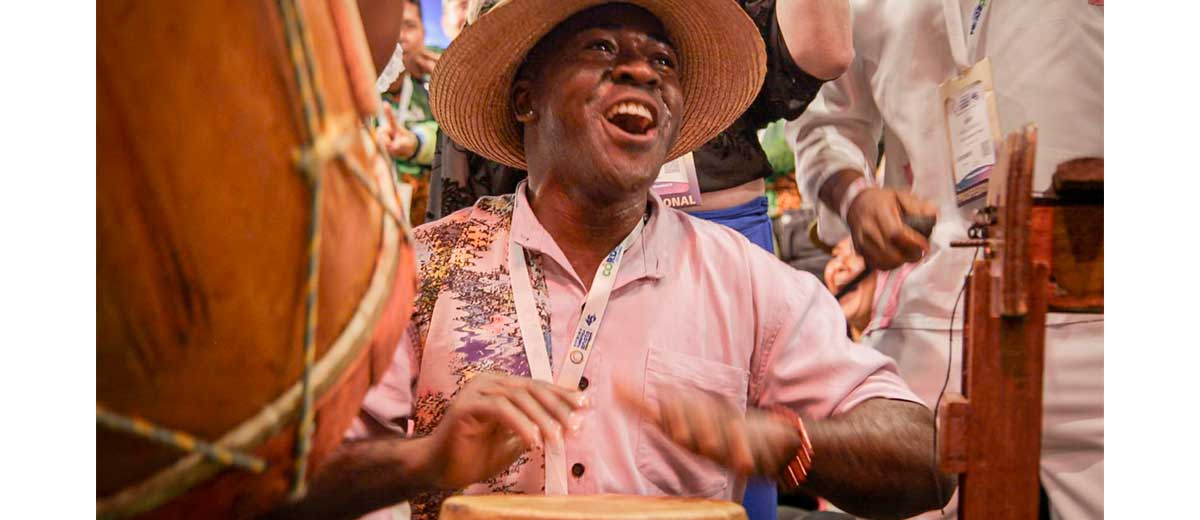 Descripción imagen: Hombre moreno tocando feliz tambores.