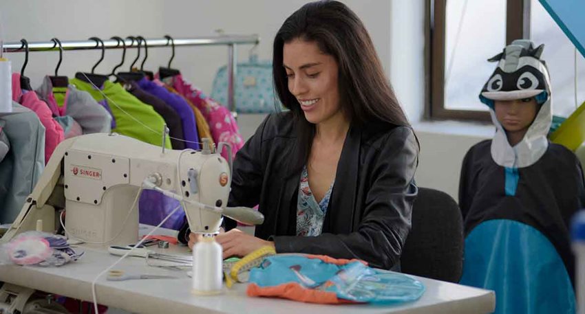 Mujer en máquina de coser produciendo ropa para niños.