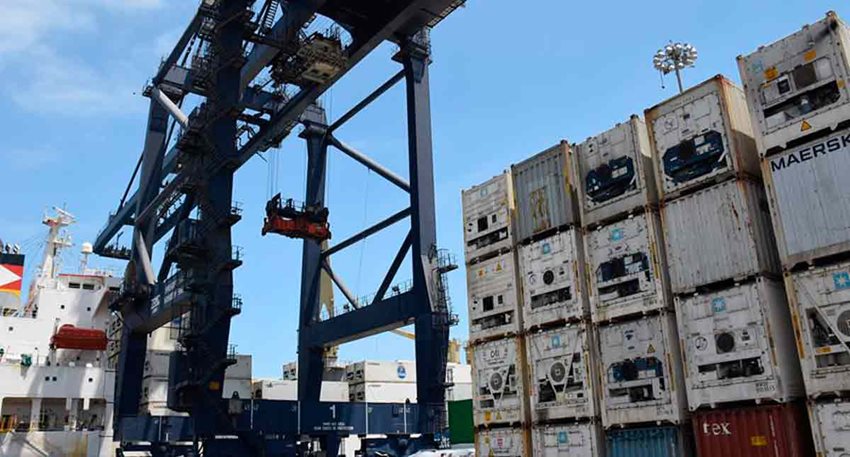 Estructura metálica azul en medio del puerto y al lado contenedores blancos descargados.