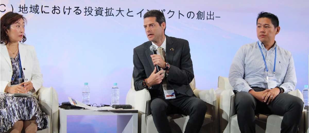 Descripción imagen: Ministro hablando por micrófono en medio de una exposición en un evento en Japón.
