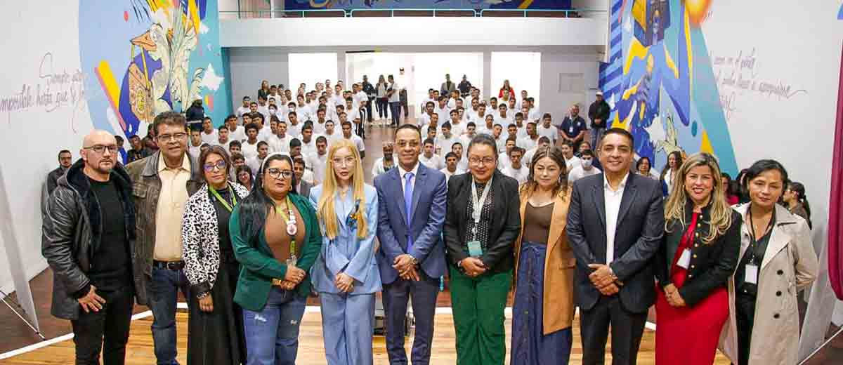 Descripción imagen: Siete mujeres y cuatro hombres posando para la foto desde el escenario y en el fondo jóvenes con overoles.