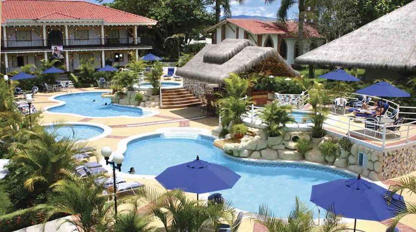 Foto panorámica, de día, de un hotel con piscinas y cabañas.