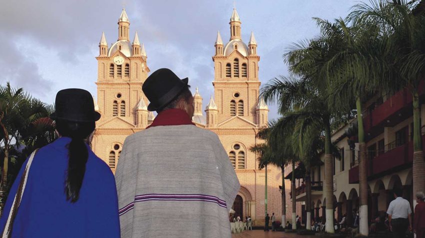 Mujer y hombre indígena de espaldas, mirando al frente una iglesia.