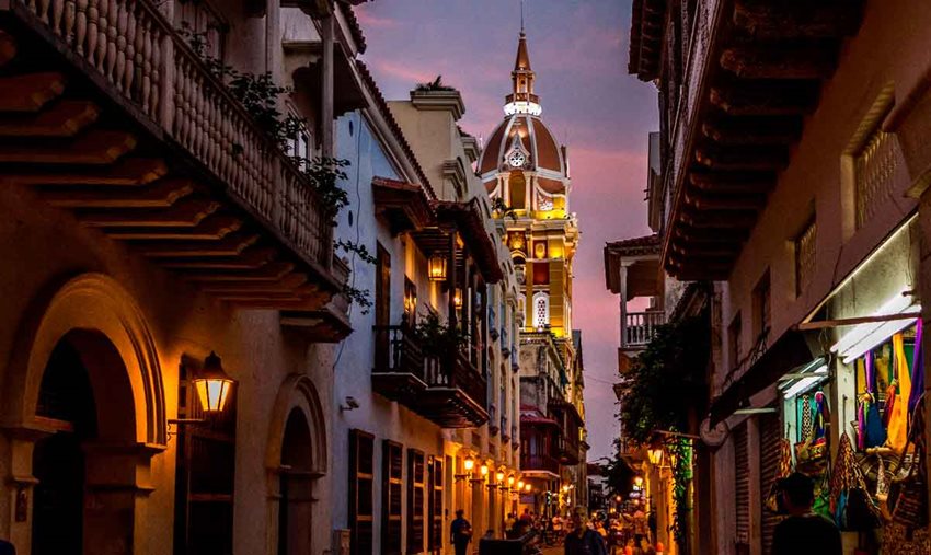 Calles del centro histórico de Cartagena, de noche, con balcones de casas y al fondo la torre del reloj.