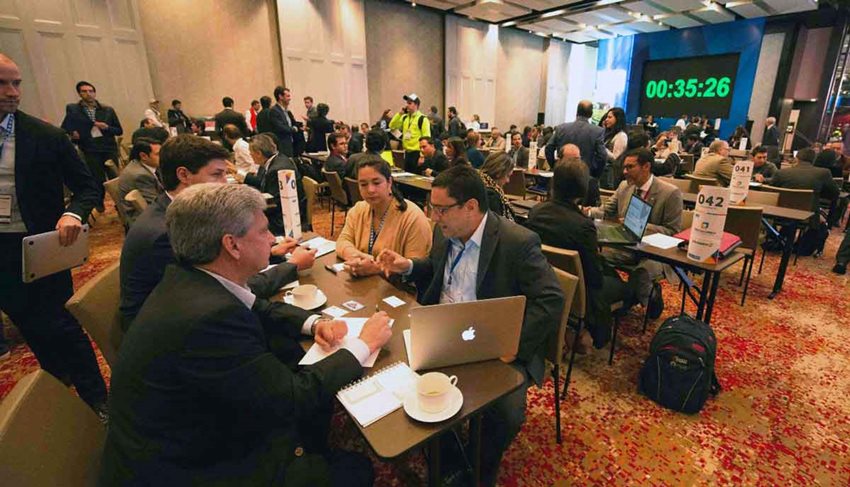 Personas sentadas en diferentes mesas, en un gran salón, conversando para negocios.