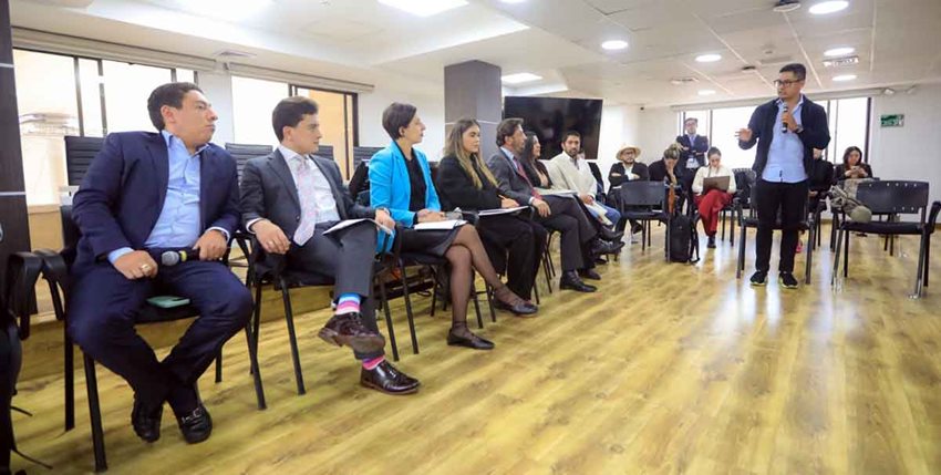 Hombres y mujeres sentados en sillas escuchando a otra persona hablarles.