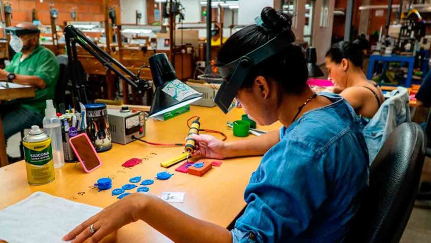 Mujer con elementos de seguridad, en taller, soldando piezas pequeñas azules.