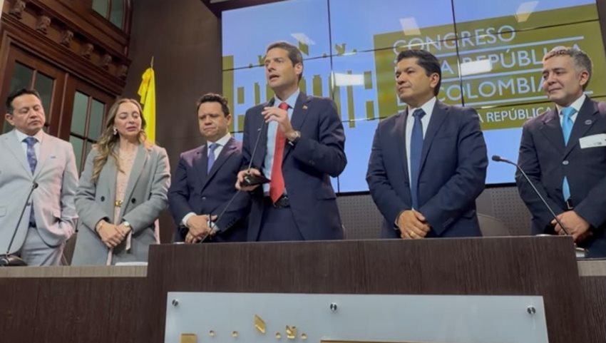 Ministro Mauricio Gómez Amín hablando a las personas, mientras está rodeado de hombres y una mujer de traje.