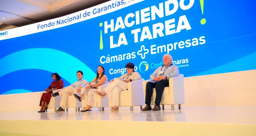 Tres mujeres y dos hombres sentados en sillas sobre el escenario, esperando que inicie la ponencia.