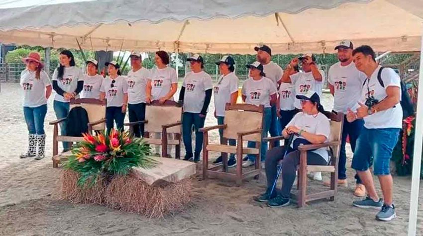 Hombres y mujeres, de pie y con camisetas blancas, debajo de una carpa mirando al frente.