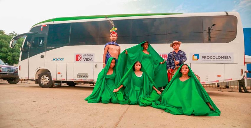 Dos hombres y cuatro mujeres wayús frente a un bus y vestidos con trajes de La Guajira.