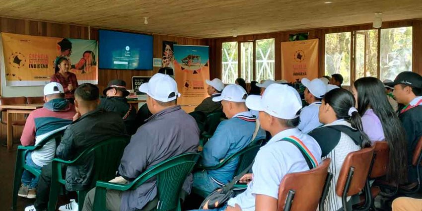 Personas, sentadas, prestando atención a mujer que habla frente a ellos.