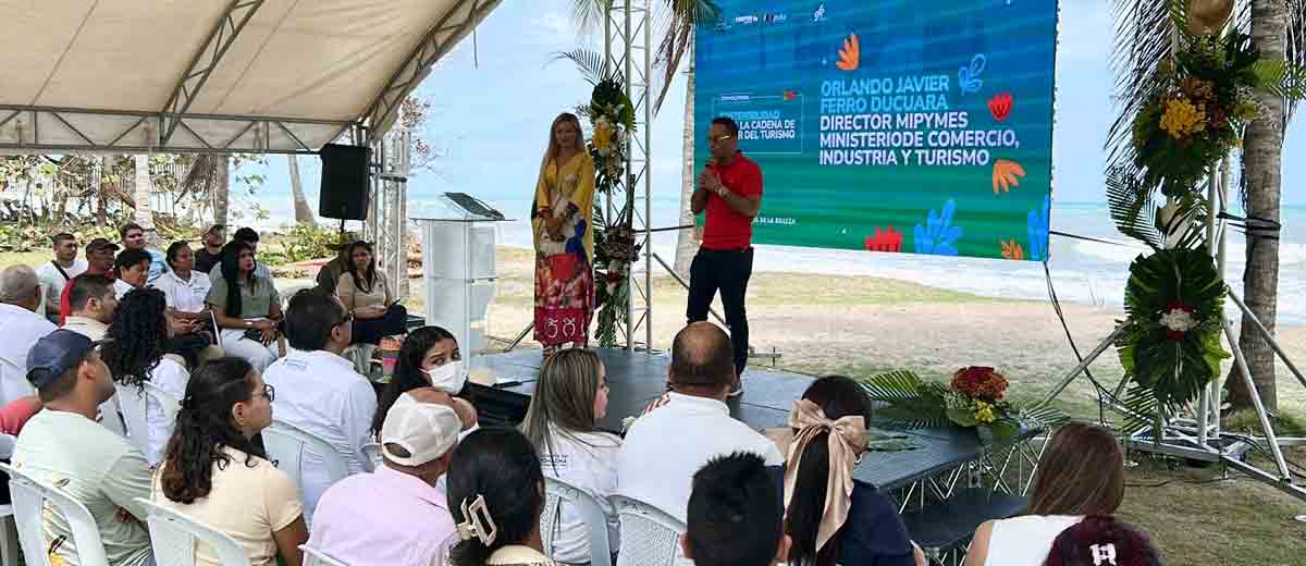 Descripción imagen: Hombre, con camisa roja, hablando por micrófono al público desde el escenario.