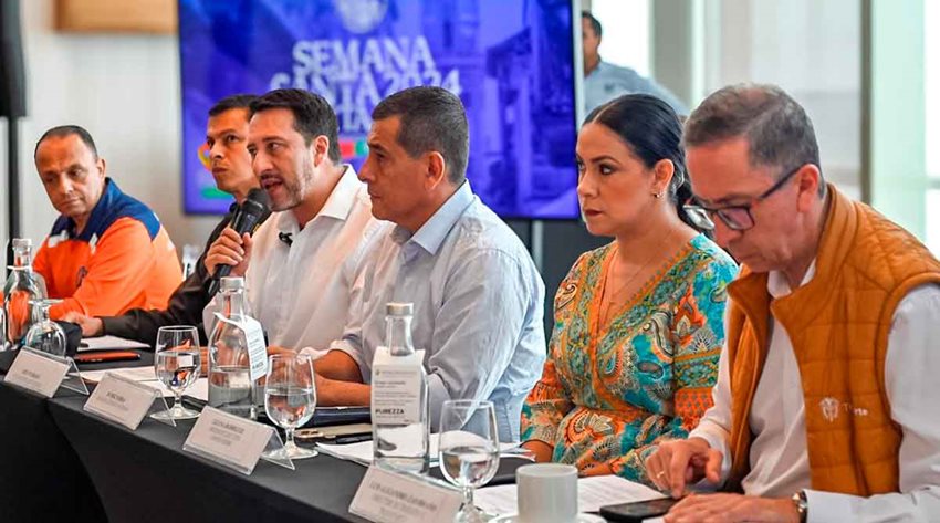 Cinco hombres y una mujer hablando al público en medio de una rueda de prensa.