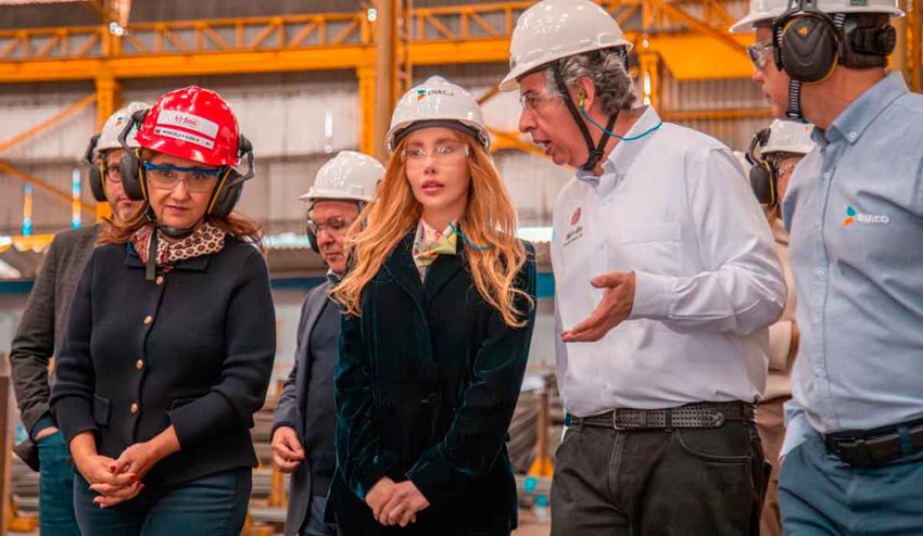 Ministra Diana Morales, con elementos de seguridad, caminando con personas por planta de producción de acero.