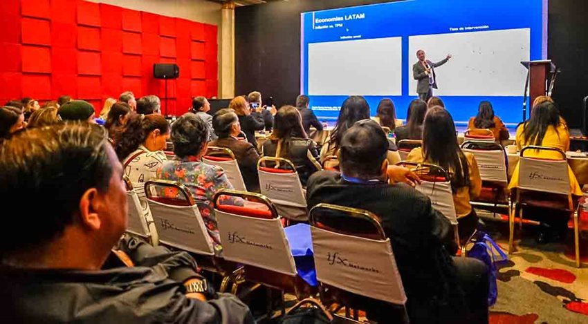 Hombres y mujeres, sentados en sillas, prestando atención al expositor en el escenario.