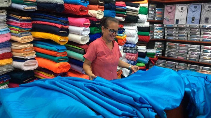 Mujer, en tienda de telas, vendiendo una tela azul que tiene tendida en las manos.