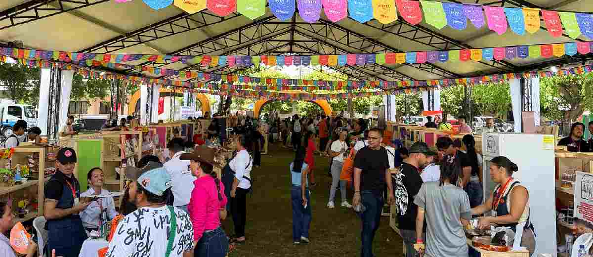 Descripción imagen: Personas caminando en medio de feria popular, con estands a los lados.