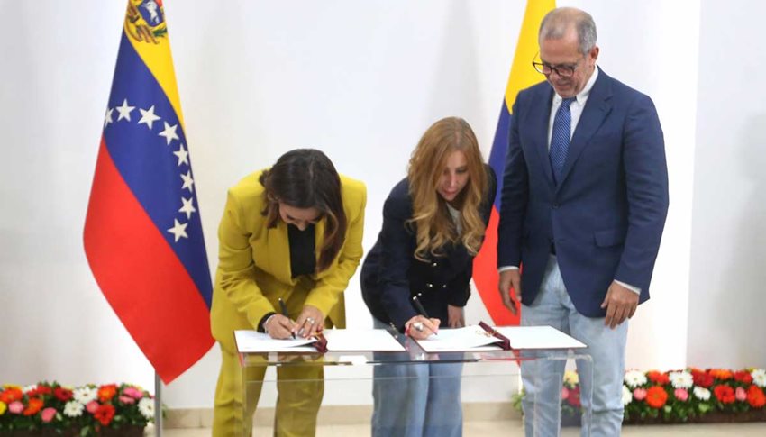 Mujeres firmando documentos sobre una mesa, mientras un hombre las mira.