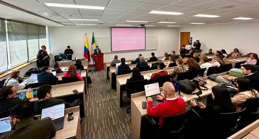 Hombres y mujeres, sentados en sillas, prestando atención al expositor en el escenario.