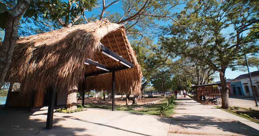 Fotografía, de día, de un parque con una casa de techo de paja en medio.