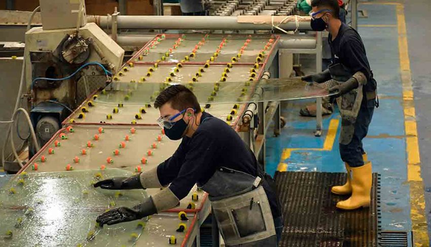 Dos jóvenes, con equipos de seguridad, cortando vidrios en taller.
