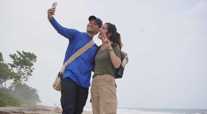 Hombre y mujer, en medio de la playa, tomándose una selfie.