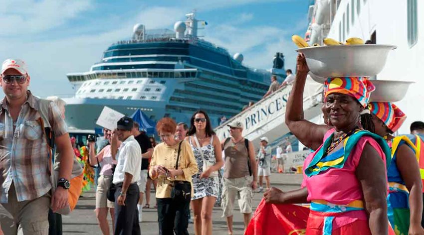 Personas bajando de un barco y caminando hacia mujeres de color con trajes típicos de la costa colombiana.
