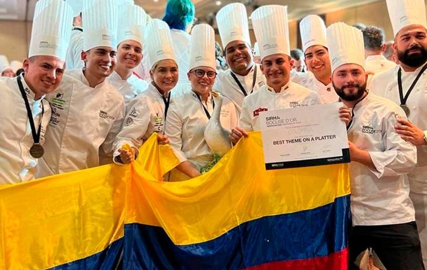 10 chefs, cada uno con su uniforme blanco, sosteniendo una bandera de Colombia.