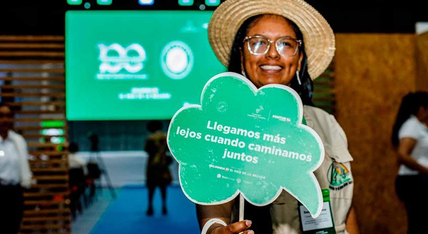 Mujer con sombrero sosteniendo cartel verde en una de sus manos.