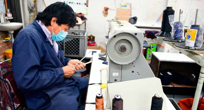 Hombre cosiendo con hilos negros y cafés, frente a máquina de coser.