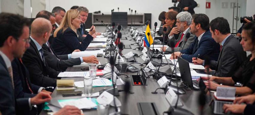 Personas sentadas en mesa rectangular, hablando en medio de una reunión.