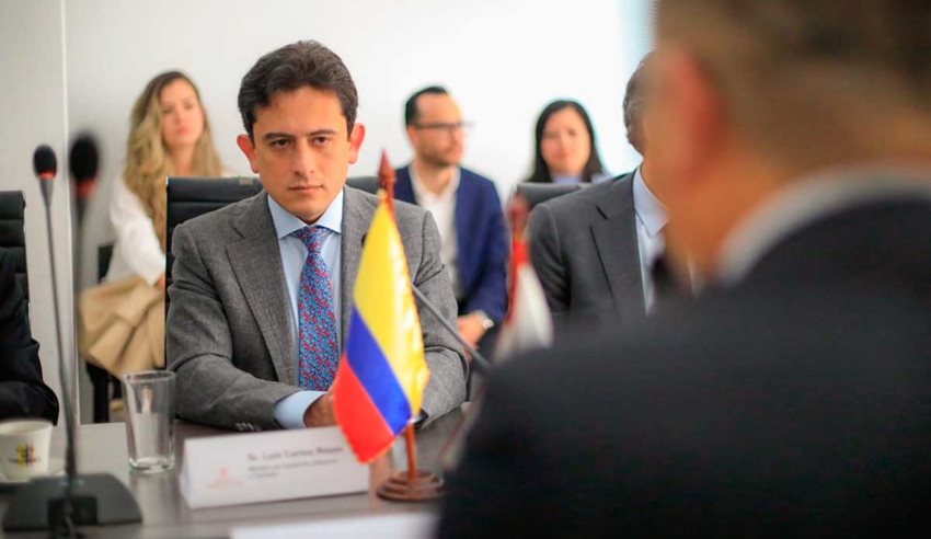 Ministro Luis Carlos Reyes reunido con comitiva de Japón y en la mitad de la mesa una bandera de Colombia.