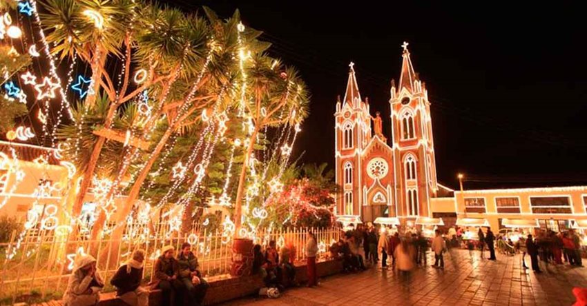Parque principal de un pueblo e iglesia iluminada en temporada navideña.
