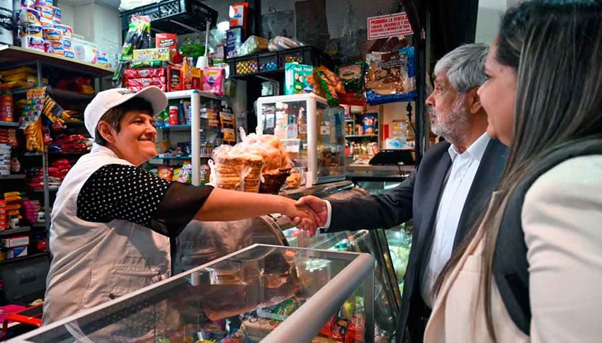 Una tendera da la mano al ministro de Comercio, los acompaña otra mujer.