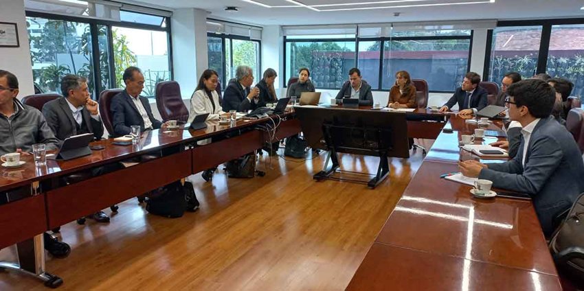 Hombres y mujeres sentados en mesa rectangular dialogando.