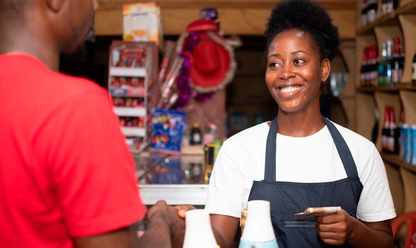 Mujer morena atendiendo una tienda de barrio y dando vueltas a un cliente.