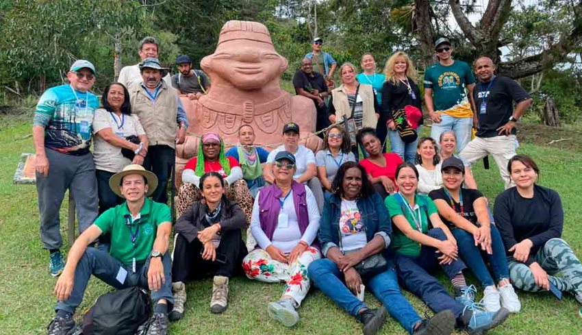 Descripción de la imagen: Hombres y mujeres posando para la foto en medio del campo y al lado de una escultura.