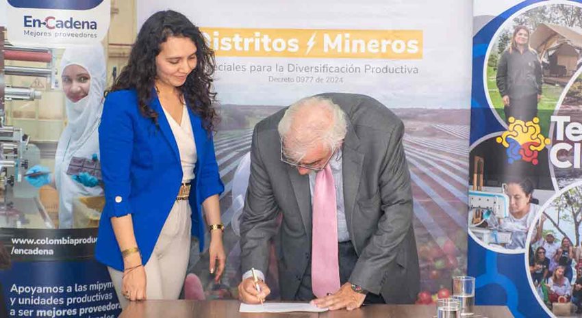 Mujer y hombre firmando documento encima de una mesa.
