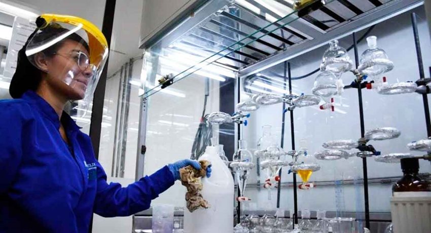 Mujer con traje de seguridad frente a elementos de laboratorio químico.
