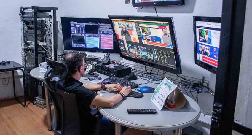 Hombre sentado en silla y escritorio, trabajando con equipos de cómputo y producción.