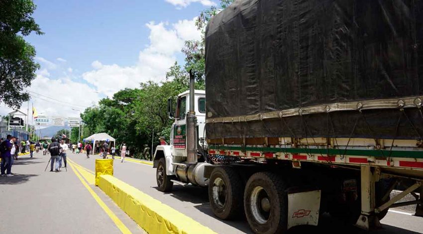 Camión blanco con tráiler negro transitando por una carretera. 